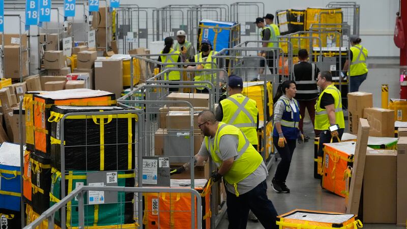 ARCHIVO - Empleados de Amazon colocan paquetes en carritos antes de cargarlos en camiones para...